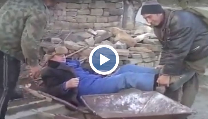 Клипът показва безмилостната борба на двама мъже, които се опитват да качат в количка за дърва своя пиян приятел