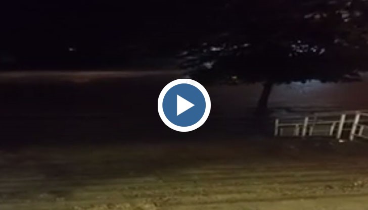 Реки от дъжд се носят по улиците отсреща, а светкавиците осветяват нощното небе