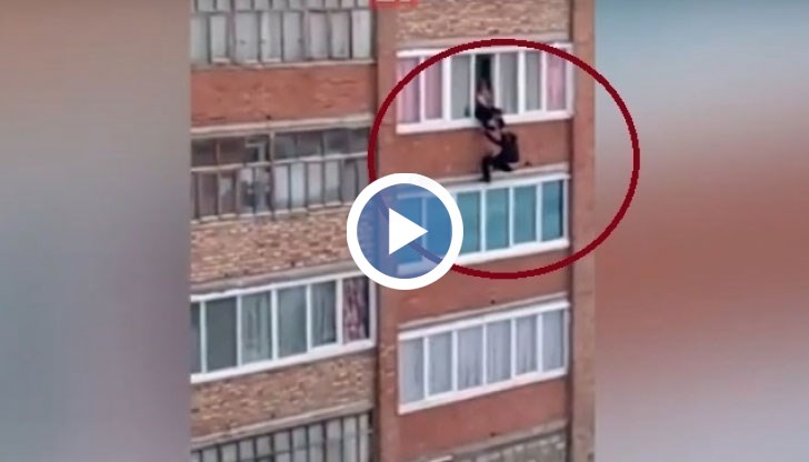Жена държи мъжа за ръцете и отчаяно се опитва да го издърпа обратно през прозореца на четвъртия етаж