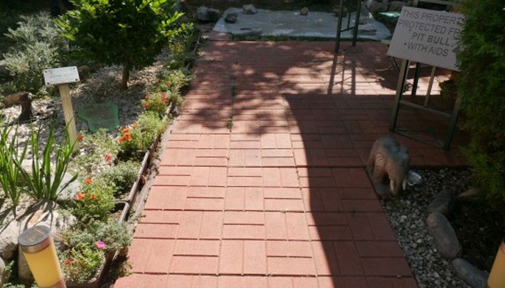 Табелата е поставена на входа на красива градинка зад блок