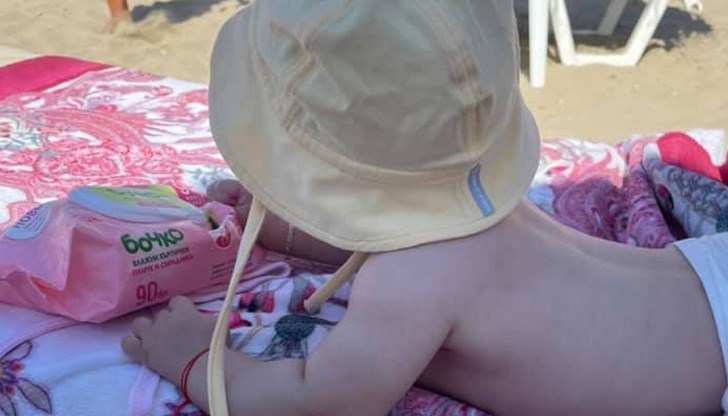 Тя постна кадър на малкото бебе, което си играе по корем на плажната хавлия